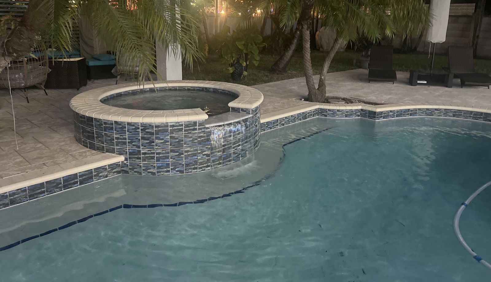 Una de sus piscinas de noche: el spa iluminado, el agua cayendo a la piscina cristalina, palmas y luces detrás