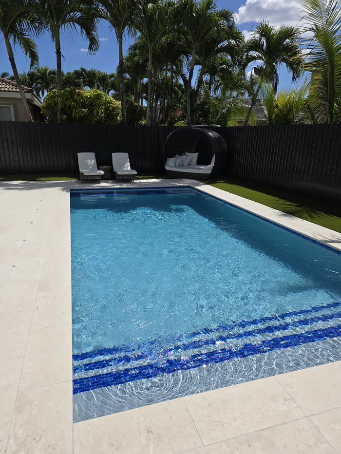 Una piscina con escalones de azulejo azul, tumbonas y palmeras