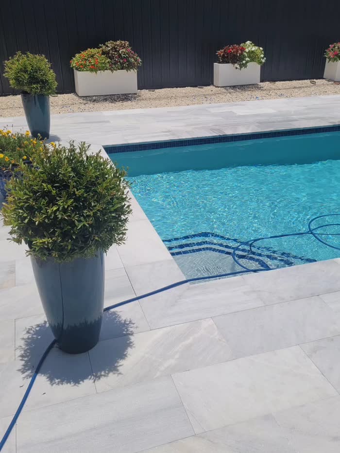 Una piscina con terraza de piedra clara y plantas en macetas