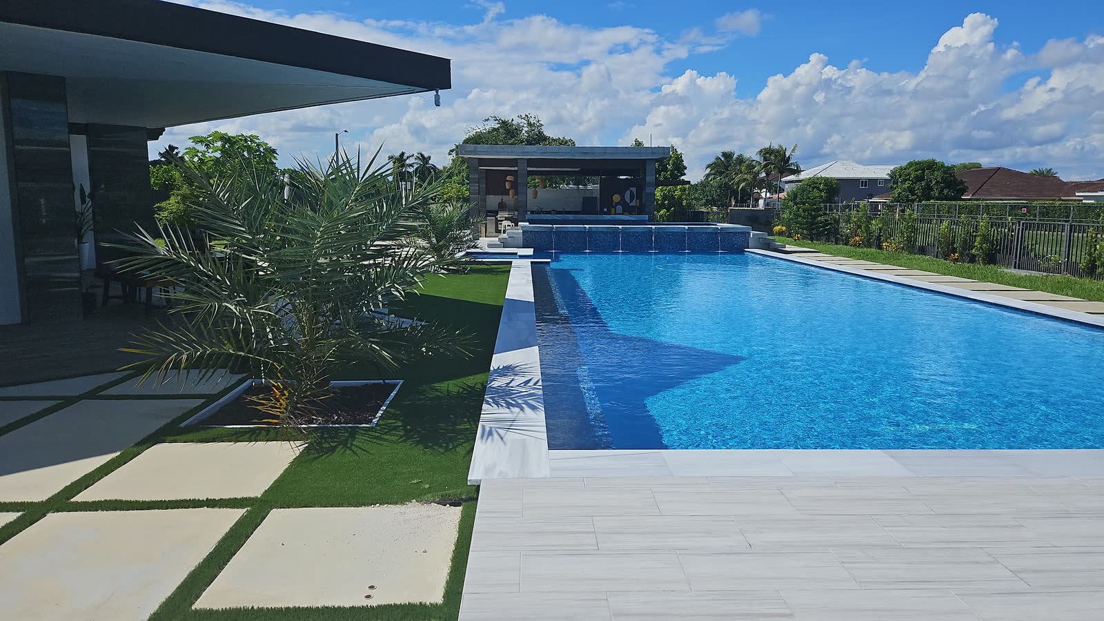Una piscina amplia y cristalina con spa y terraza de césped y adoquines